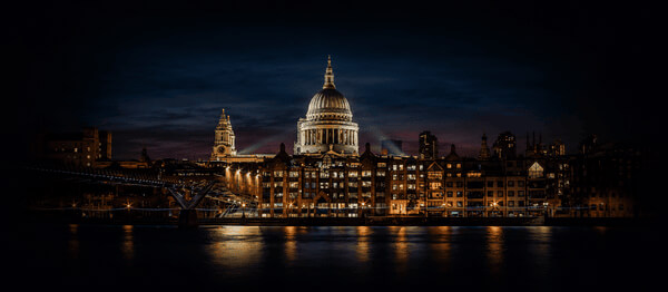 A river skyline at dusk with a domed landmark building lit against the evening sky.